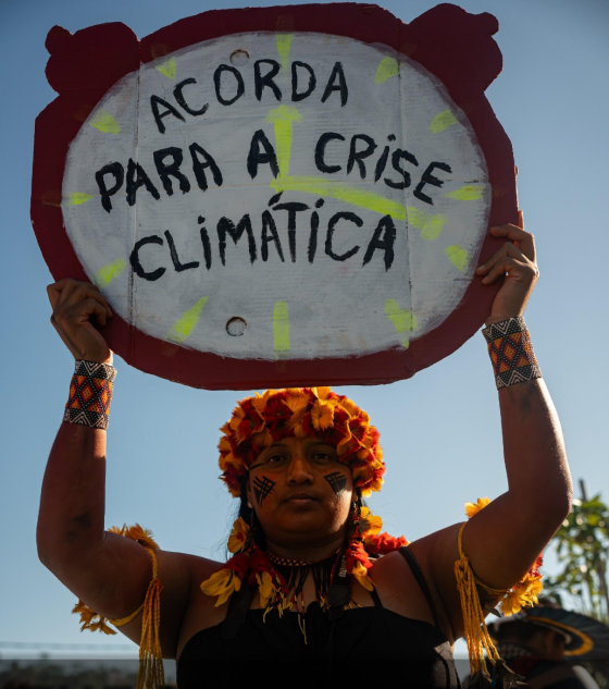 The Money Trail- Cover: Indigenous woman holding climate clock