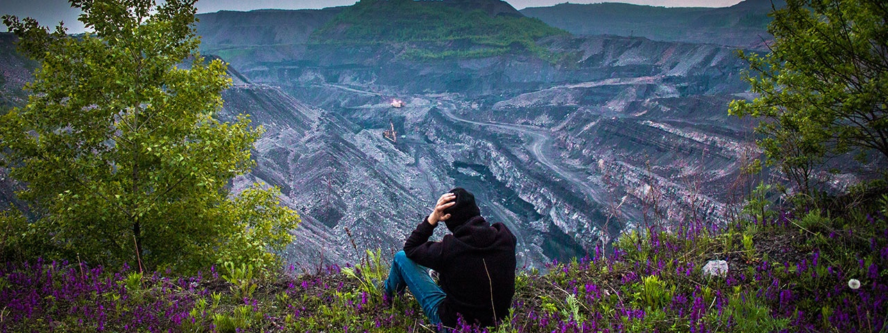 Man, sitting on the edge of a giant coal mine and looking into the mine