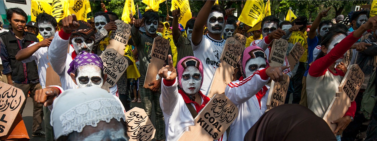 Group of protesters in Bangladesh with painted faces, holding signs that say „coal kills“